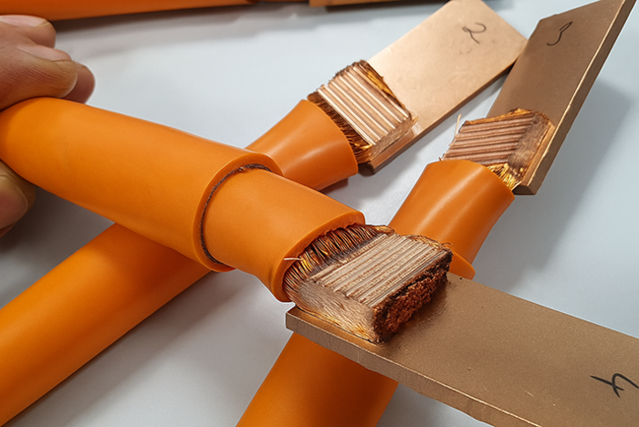 Orange-isolated copper cables with exposed stranded ends connected to flat copper busbars.